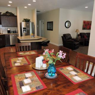 A cozy dining area with a wooden table set for four, featuring a centerpiece of flowers, adjacent to an open kitchen and living space.