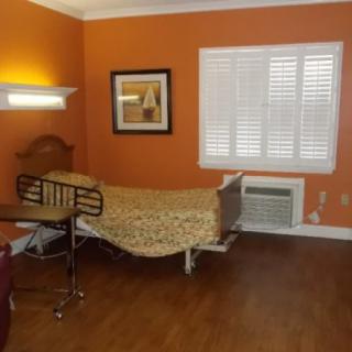 A well-lit room with orange walls, featuring a single bed, a window with shutters, and a piece of artwork on the wall.