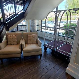 A cozy hotel lobby corner with armchairs and a luggage cart near large windows.