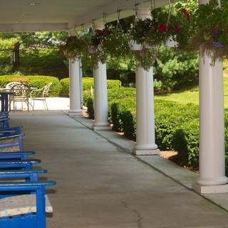 A porch with columns and blue chairs overlooking a garden.