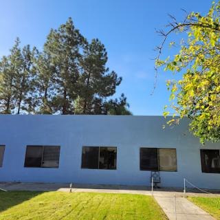 A serene view of a blue building surrounded by trees and a well-manicured lawn.