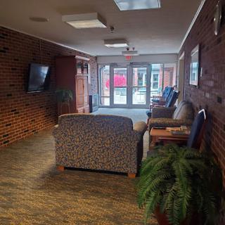 A cozy lobby area with comfortable seating and a brick wall, inviting natural light from the entrance.