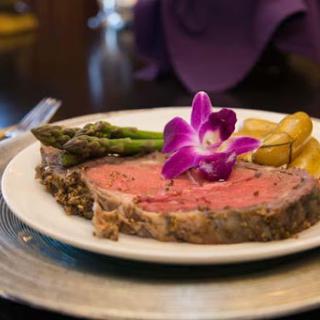 A beautifully plated dinner featuring a juicy steak, asparagus, and a decorative purple flower.