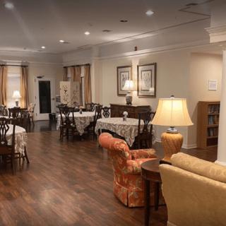 A cozy dining area with tables, chairs, and warm lighting on hardwood flooring.