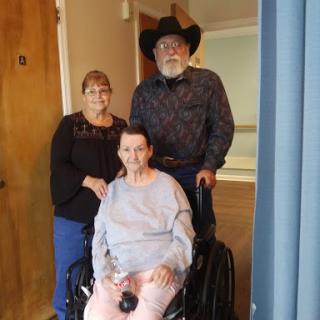 A family portrait featuring a smiling woman in a wheelchair, accompanied by two supportive individuals.