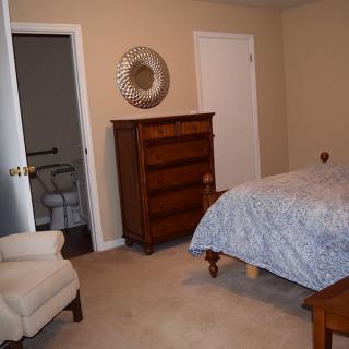 A cozy bedroom with a dresser, bed, and armchair.