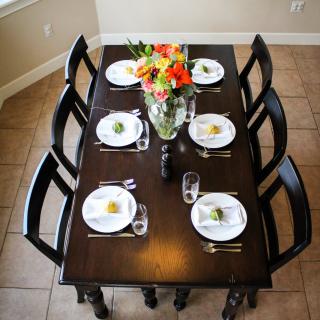 A dining table set for six people with elegant white plates, cutlery, and a floral centerpiece.