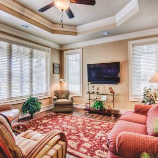 A cozy living room with a sofa, armchair, and TV, featuring large windows and decorative accents.