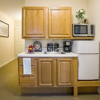 A small kitchenette with wooden cabinets, a microwave, refrigerator, and coffee maker.