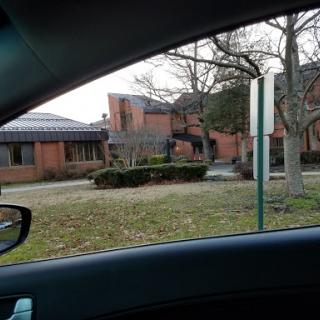A view of a brick building from inside a car, framed by trees and a road sign.