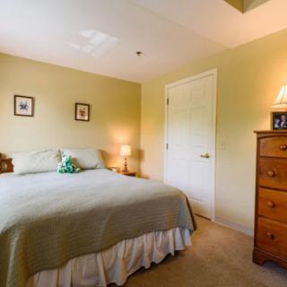 Cozy bedroom with a neatly made bed, wooden chest of drawers, and warm lighting.