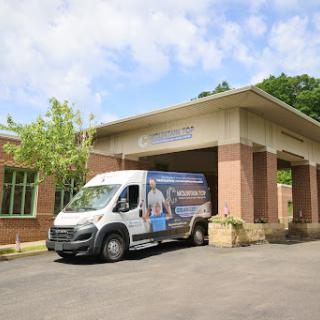 A delivery van parked in front of a modern building under a partly cloudy sky.