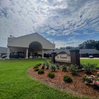 A welcoming entrance to a modern facility, surrounded by lush landscaping under a cloudy sky.