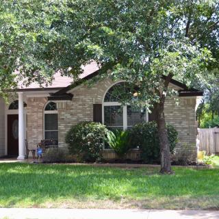 A suburban brick house with a front yard and trees.