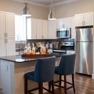 A modern kitchen with white cabinets, a stainless steel refrigerator, and an island with two blue chairs.