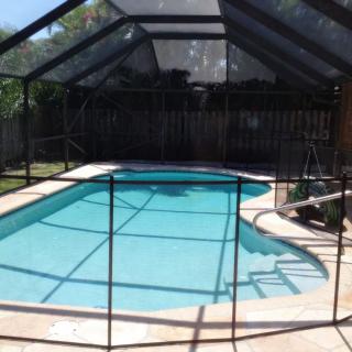 A fenced swimming pool with a screen enclosure on a sunny day.
