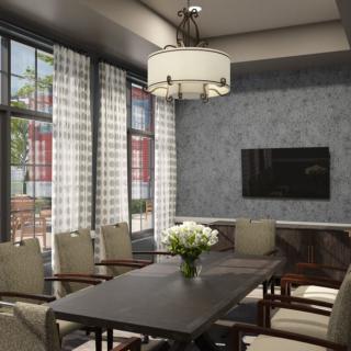 A modern conference room with a large meeting table, chairs, and a wall-mounted television. The room features large windows allowing natural light, a stylish chandelier, and a vase of flowers on the table.