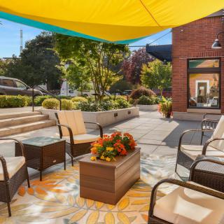 A cozy outdoor patio with comfortable seating under a large, colorful umbrella shade.