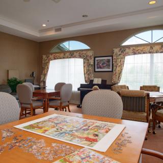 A cozy living room with tables and chairs, featuring a partially completed puzzle.