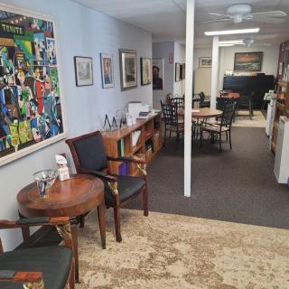 A cozy office interior with a waiting area featuring chairs, tables, artwork on the walls, and a bookshelf.