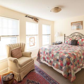 A cozy bedroom with a patterned bedspread, comfortable armchair, and large windows allowing natural light.