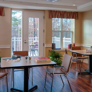 A cozy dining area with several tables and chairs, featuring large windows allowing natural light to illuminate the space.