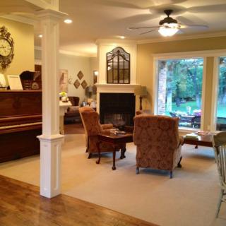 A cozy living room featuring a fireplace, piano, and elegant furniture with large windows overlooking the garden.
