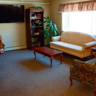 A cozy living room with a sofa, armchair, coffee table, and a bookshelf under a wall-mounted TV.