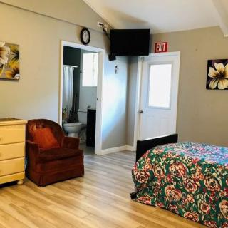 A cozy bedroom with a colorful bedspread, wooden dresser, and an armchair next to a door leading to a bathroom.