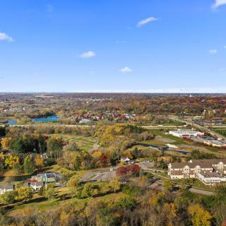 Aerial view of a picturesque countryside landscape during autumn, featuring trees, buildings, and a clear blue sky.