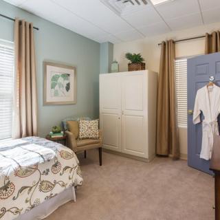 A cozy bedroom with soft tones, featuring a bed, armchair, and wardrobe.