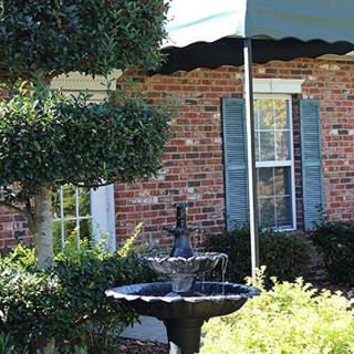 A charming brick house with blue shutters, surrounded by lush greenery and featuring a quaint fountain in the front yard.