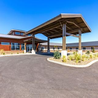 A modern building entrance with a covered driveway and landscaped surroundings under a clear blue sky.