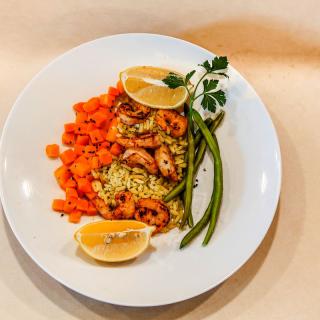 A beautifully plated dish featuring shrimp over rice, accompanied by diced carrots, green beans, and lemon slices.