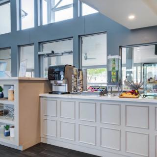 A modern cafe interior featuring a coffee machine, countertop with fruits, and display shelves.
