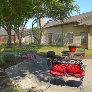 A peaceful outdoor patio area with red-cushioned chairs and tables surrounded by trees.