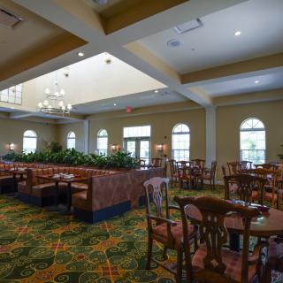 A spacious dining area with elegant chandeliers, carpeted flooring, and neatly arranged tables and chairs.