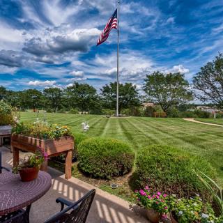 A well-maintained garden with a patio and an American flag under a vibrant, cloudy sky.