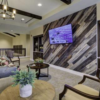 A modern living room with a wood accent wall, mounted television, elegant furniture, and a decorative chandelier.