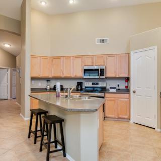 A modern kitchen with an island and bar stools, featuring wooden cabinets and stainless steel appliances.