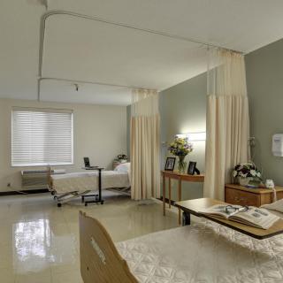 A clean and organized hospital room with two beds, separated by curtains, and a window letting in natural light.