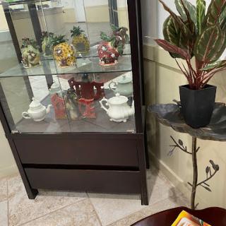 A stylish display cabinet showcasing colorful teapots and decorative items, complemented by a potted plant in the corner.