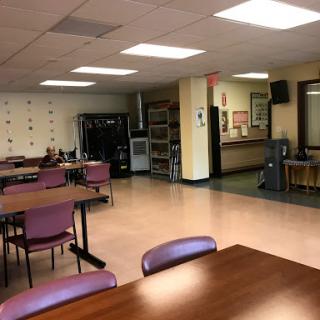 A spacious dining area with tables and chairs, equipped with a kitchenette in the background.