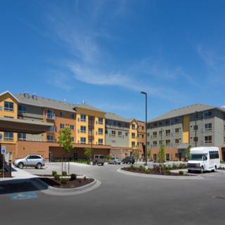A modern residential complex with multiple buildings and a parking area under a clear blue sky.
