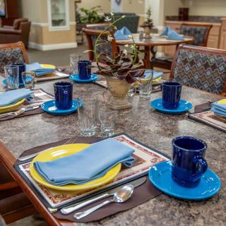 A neatly arranged dining table with blue cups, yellow plates, and napkins.