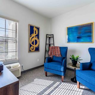 A cozy living room with two blue armchairs, decorated with musical artwork and illuminated by natural light from a window.