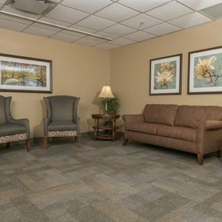 A comfortable waiting area featuring a sofa, two chairs, a lamp, and framed artwork on the walls.