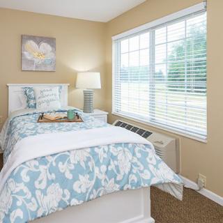 A cozy bedroom with floral bedding and a large window, allowing natural light to fill the space.