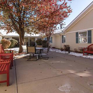 A peaceful courtyard with benches and patio furniture under a tree with autumn leaves.