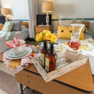 A cozy bedroom setup with a breakfast tray featuring flowers, drinks, and decor.